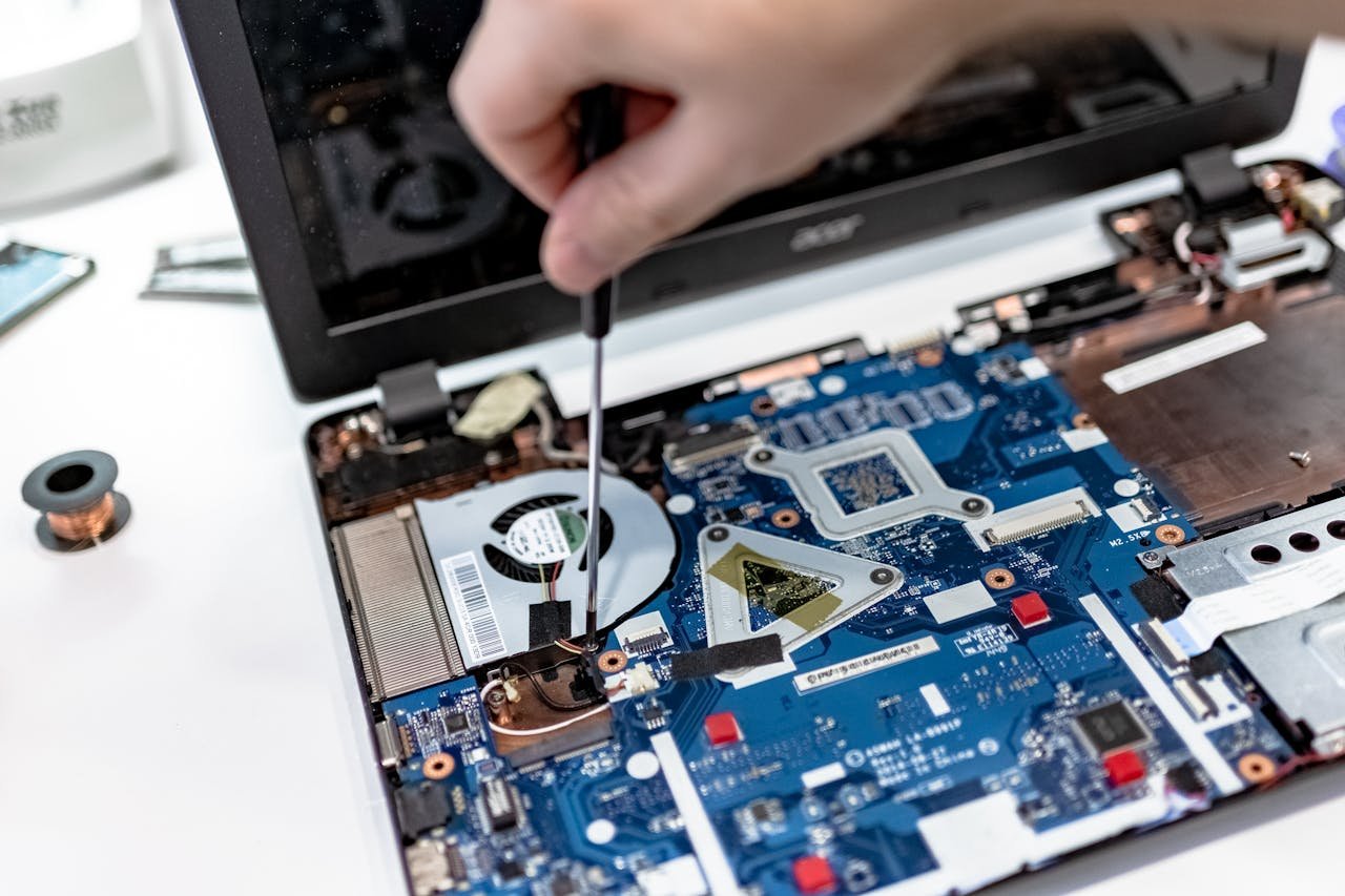 Home Hand repairing a laptop motherboard with a screwdriver, highlighting tech maintenance.